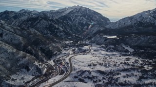 AX126_235E - 5.5K aerial stock footage approach road at the base of snowy mountains in winter, Wasatch Range, Utah