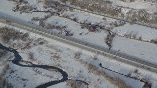 AX127_010 - 5.5K aerial stock footage of tracking white car and black truck on country highway with winter snow, Heber City, Utah