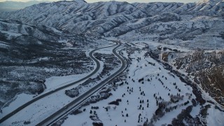 AX127_053E - 5.5K aerial stock footage approach and follow I-80 with light traffic through a wintery Wasatch Range pass at sunset, Utah
