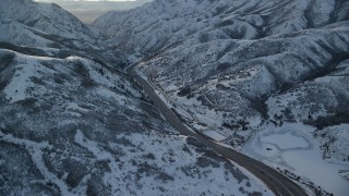 AX127_057 - 5.5K aerial stock footage approach I-80 through a snowy mountain pass in wintertime at sunset, Wasatch Range, Utah