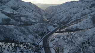 AX127_060 - 5.5K aerial stock footage of a curve in the freeway through a snowy Wasatch Range mountain pass at sunset, Utah