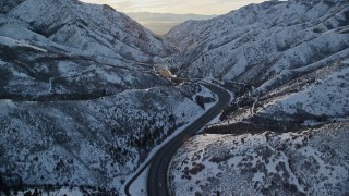 AX127_060E - 5.5K aerial stock footage of a curve in the freeway through a snowy Wasatch Range mountain pass at sunset, Utah