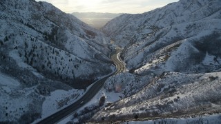 AX127_064 - 5.5K aerial stock footage approach freeway through the Wasatch Range with winter snow at sunset, Utah