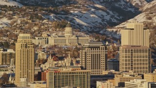 AX127_101E - 5.5K aerial stock footage of Utah State Capitol seen between Downtown Salt Lake City buildings at sunset in wintertime