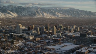 AX127_145 - 5.5K stock footage aerial video orbit of Downtown Salt Lake City and distant snow mountains at sunset in winter, Utah