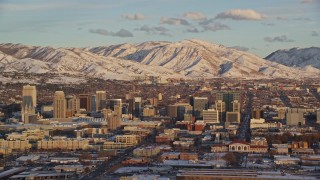 AX127_151E - 5.5K aerial stock footage of downtown area of Salt Lake City and snowy mountains at sunset, Utah