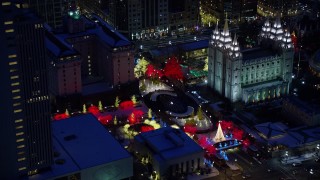 AX128_080 - 5.5K stock footage aerial video orbit fountain and trees lit for Christmas at Salt Lake Temple with snow at night, Downtown Salt Lake City, Utah