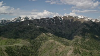 AX130_060E - 5.5K aerial stock footage of flying by snowy peaks, green ridges, Oquirrh Mountains, Utah
