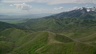 AX130_062E - 5.5K aerial stock footage of flying over green ridges, approaching snowy peaks, Oquirrh Mountains, Utah