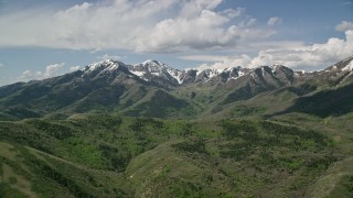 AX130_065E - 5.5K aerial stock footage of flying by snowy peaks, green ridges, Oquirrh Mountains, Utah