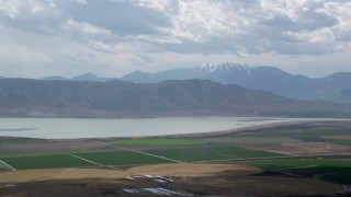 AX130_083 - 5.5K aerial stock footage of a view of circular crop fields, distant snow-capped peak and Utah Lake, Utah