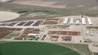 AX130_102 - 5.5K aerial stock footage of passing by greenhouses, ponds, near circular crop fields, Elberta, Utah