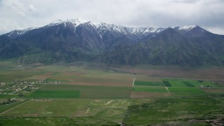 AX130_114 - 5.5K aerial stock footage of passing by small rural town, farm fields, Wasatch Range, Mona, Utah