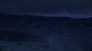 AX130_127_DFN - Aerial stock footage of 4K day for night color corrected aerial footage of flying by hills, trees, heavy clouds above, Wasatch Range, Utah