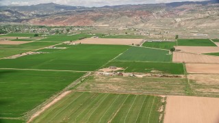 AX130_192E - 5.5K aerial stock footage of lying by farmhouse and green fields, Richfield, Utah