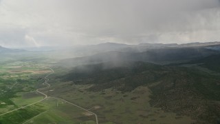 AX130_215 - 5.5K aerial stock footage of flying by rain falling on mountains, trees, near farming community, Fishlake National Forest, Utah