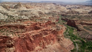 AX130_266 - 5.5K stock footage aerial video of flying by Waterpocket fold rock formations, desert road through a canyon, Capitol Reef National Park, Utah