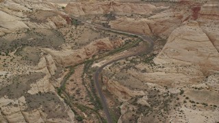 AX130_298E - 5.5K aerial stock footage of passing by desert road through Waterpocket Fold rock formations, mesas, Capitol Reef National Park, Utah