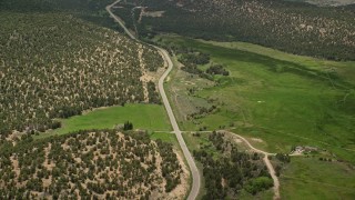 AX130_364E - 5.5K aerial stock footage of flying by Route 12, green fields, hills covered in vegetation, tilt to reveal small town, Boulder, Utah