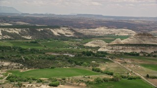 AX130_371E - 5.5K aerial stock footage of small mountains, green fields, rural town around a pond, Boulder, Utah