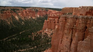 AX130_463 - 5.5K stock footage aerial video of flying by hoodoos on mesa cliffs, tree-covered canyon, Bryce Canyon National Park, Utah
