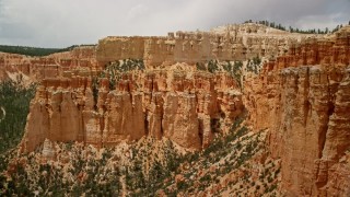AX130_464E - 5.5K aerial stock footage of flying away from hoodoos, mesa cliff, tree-covered slopes, Bryce Canyon National Park, Utah