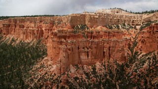 AX130_465 - 5.5K stock footage aerial video of flying away from hoodoos, mesa cliff, tree-covered slopes, Bryce Canyon National Park, Utah
