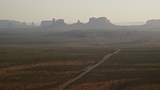AX133_100E - 5.5K aerial stock footage of wide view of highway leading to buttes and mesas in Monument Valley, Utah, Arizona, twilight