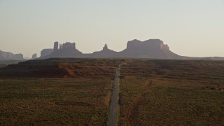 AX133_110E - 5.5K aerial stock footage of flying toward buttes, following highway in Monument Valley, Utah, Arizona, twilight