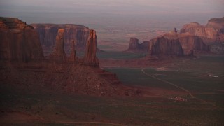 AX133_177E - 5.5K aerial stock footage of passing by Three Sisters and Rain Got Mesa, Monument Valley, Utah, Arizona, sunset