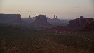 AX133_189E - 5.5K aerial stock footage of an approach to West Mitten Butte and Merrick Butte, Monument Valley, Utah, Arizona, sunset