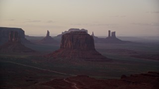 AX133_192E - 5.5K aerial stock footage of flying by buttes in a hazy desert valley, Monument Valley, Utah, Arizona, sunset