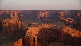 AX133_199E - 5.5K aerial stock footage of flying by rock formations and Hunt's Mesa, Monument Valley, Utah, Arizona, sunset