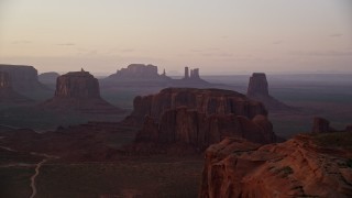 AX133_215E - 5.5K aerial stock footage pass by buttes in a hazy desert valley, Monument Valley, Utah, Arizona, twilight