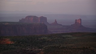 AX133_223E - 5.5K aerial stock footage of mesas and buttes in the hazy valley, Monument Valley, Utah, Arizona, twilight