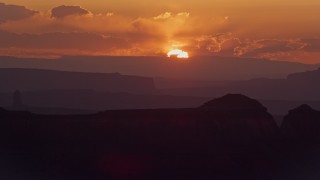 AX134_008E - 5.5K aerial stock footage of passing by sun setting behind a mesa, Monument Valley, Utah, Arizona, sunset