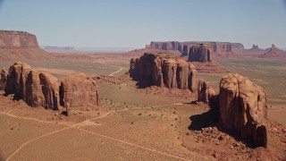AX135_030 - 5.5K aerial stock footage of approaching three buttes in a hazy desert valley, Monument Valley, Utah, Arizona