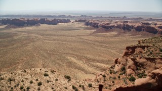 AX135_166 - 5.5K aerial stock footage of flying over Hunt's Mesa to approach a desert valley, Monument Valley, Utah, Arizona