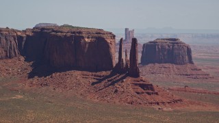 AX135_184 - 5.5K aerial stock footage of flying by a mesa and buttes in a hazy desert valley, Monument Valley, Utah, Arizona