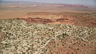 AX135_188E - 5.5K aerial stock footage of flying over Mitchell Mesa, approaching a wide desert valley, Monument Valley, Utah, Arizona