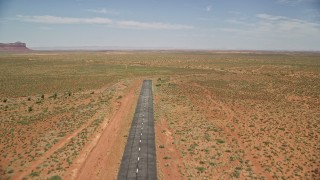 AX136_001 - 5.5K aerial stock footage of flying over a runway toward wide desert valley, Monument Valley Airport, Utah