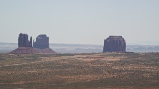 AX136_004E - 5.5K aerial stock footage of passing tall buttes and a hazy desert valley, Monument Valley, Utah, Arizona