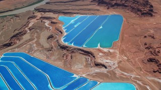AX136_273E - 5.5K aerial stock footage of flying away from potash ponds in an arid desert valley, Moab, Utah