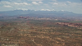 AX137_006E - 5.5K aerial stock footage of a wide view of rock formations, snow-capped mountains, Arches National Park, Utah