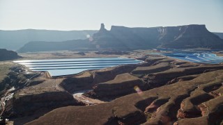 AX138_062 - 5.5K aerial stock footage of sun shining on potash ponds with butte and mesa behind them, Moab, Utah