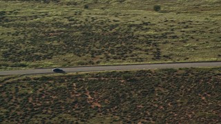 AX138_122E - 5.5K aerial stock footage track sedan on desert road through Canyonlands National Park, Utah