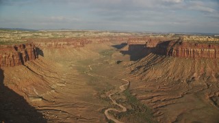 AX138_248E - 5.5K aerial stock footage of flying by dry riverbed in a wide desert canyon, Moab, Utah