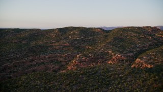 AX138_391E - 5.5K aerial stock footage of flying over hill, revealing Castle Valley and buttes in distance, Moab, Utah, sunset