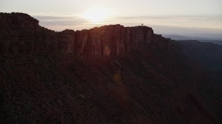 AX138_393E - 5.5K aerial stock footage of the sun setting behind mesa cliffs, Moab, Utah, sunset