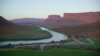 AX138_400 - 5.5K stock footage aerial video of flying by Red Cliffs Lodge and Colorado River with view of Parriott Mesa, Moab, Utah, sunset